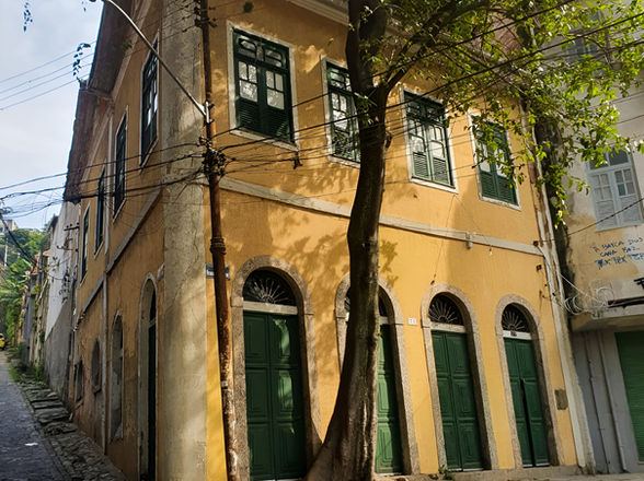 Esquina do casarão amarelo do Espaço Mova, com portas verdes em arco e árvore na calçada